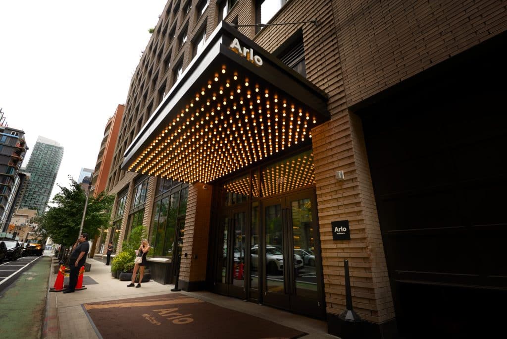Arlo Midtown hotel entrance featuring modern architecture, illuminated marquee, and stylish decor, with guests arriving and a vibrant Manhattan streetscape.