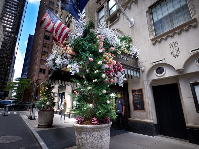 Elegant entrance of The Benjamin Royal Sonesta New York, featuring floral arrangements and American flag, showcasing luxury accommodations in Midtown Manhattan.