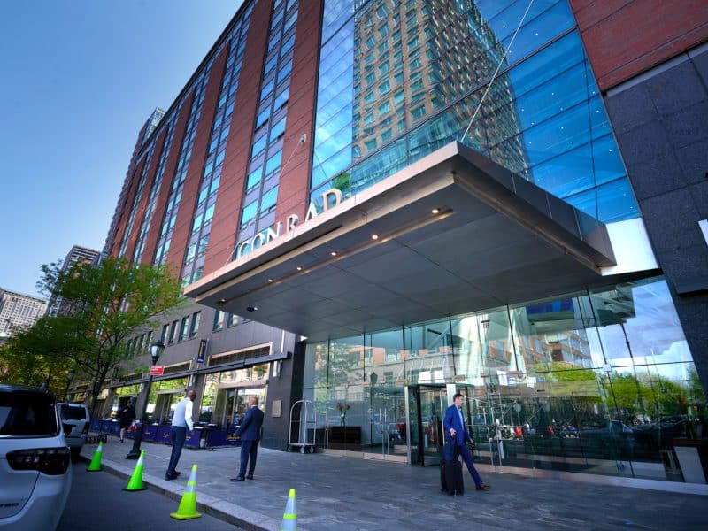 Conrad New York Downtown hotel exterior, featuring modern glass facade, entrance awning, and guests arriving, highlighting luxury accommodations in Lower Manhattan.