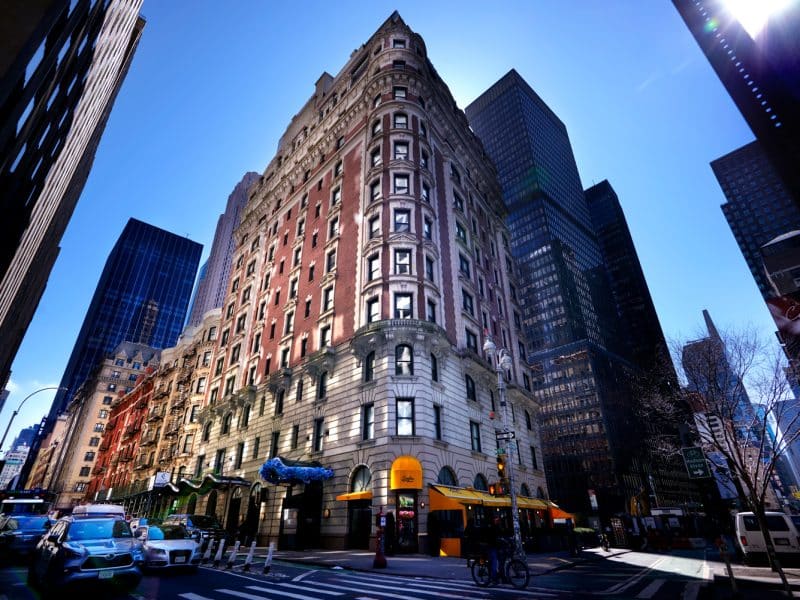 Historic building exterior of Dream Midtown hotel, showcasing elegant architecture, surrounded by modern skyscrapers in Manhattan's Financial District.
