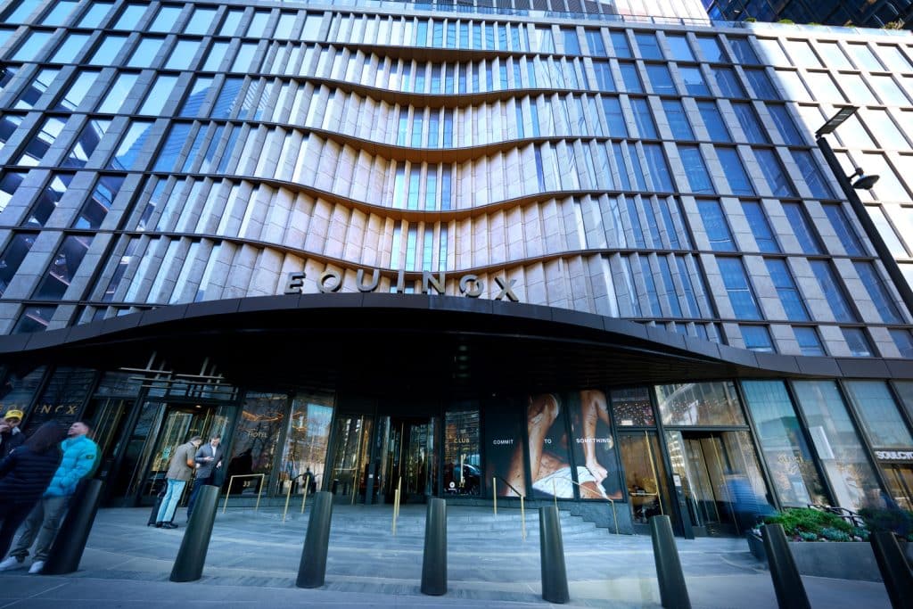 Equinox Hotel at Hudson Yards entrance featuring modern architecture, sleek design, and wellness branding, with guests arriving and interacting in a vibrant urban setting.