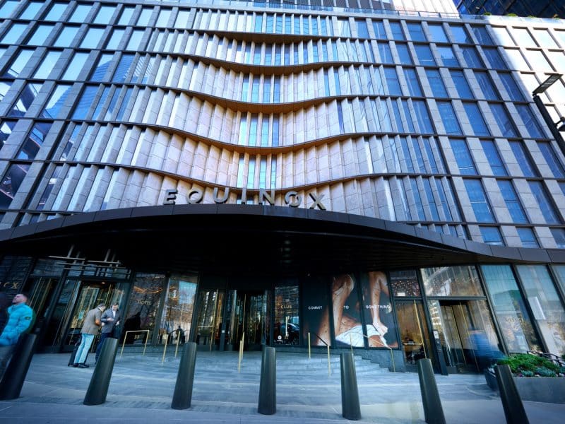 Equinox Hotel entrance at Hudson Yards, featuring modern architectural design, prominent "EQUINOX" signage, and guests interacting outside.