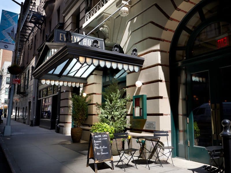 Evelyn Hotel entrance featuring elegant awning, outdoor seating, and signage for Evelyn Café, located in Manhattan’s NoMad neighborhood.