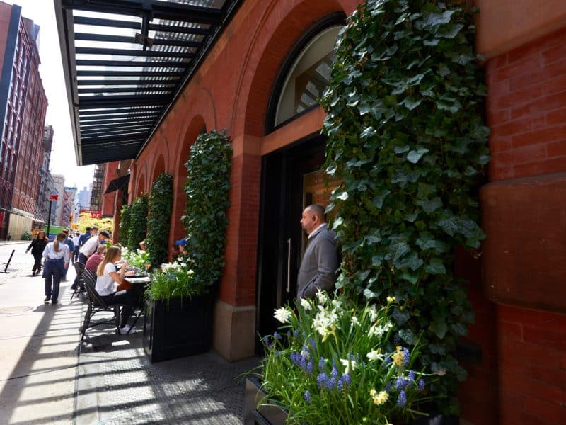 Exterior view of The Mercer Hotel in SoHo, New York City, featuring lush greenery, outdoor seating, and a stylish entrance, highlighting the hotel's boutique luxury and vibrant neighborhood atmosphere.
