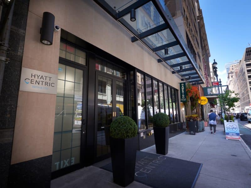 Hyatt Centric Midtown 5th Avenue hotel entrance with modern design, large windows, greenery, and signage, located in Manhattan near key attractions.