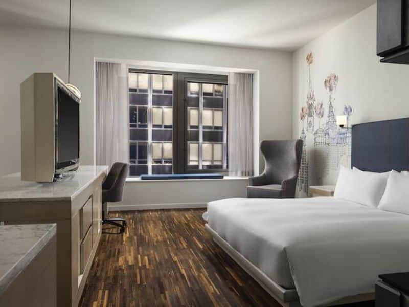 Modern hotel room at Hyatt Centric Wall Street featuring a queen bed, work desk, TV, and large window with city views.