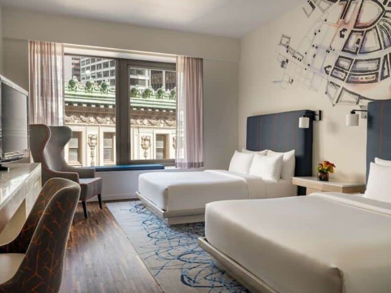 Modern hotel room at Hyatt Centric Wall Street featuring two beds, desk area, large window with city view, and contemporary decor.