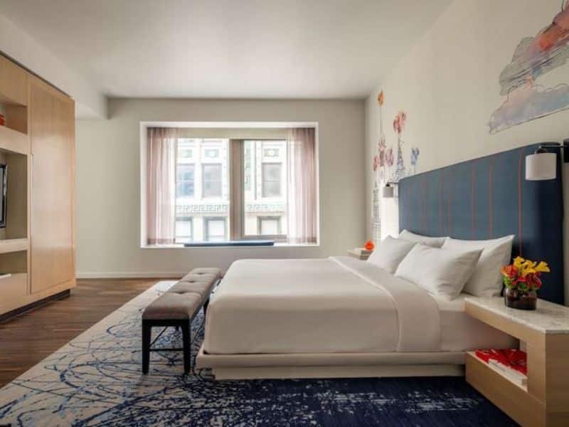 Modern hotel room at Hyatt Centric Wall Street featuring a king bed, stylish decor, large windows with city views, and a cozy seating area.