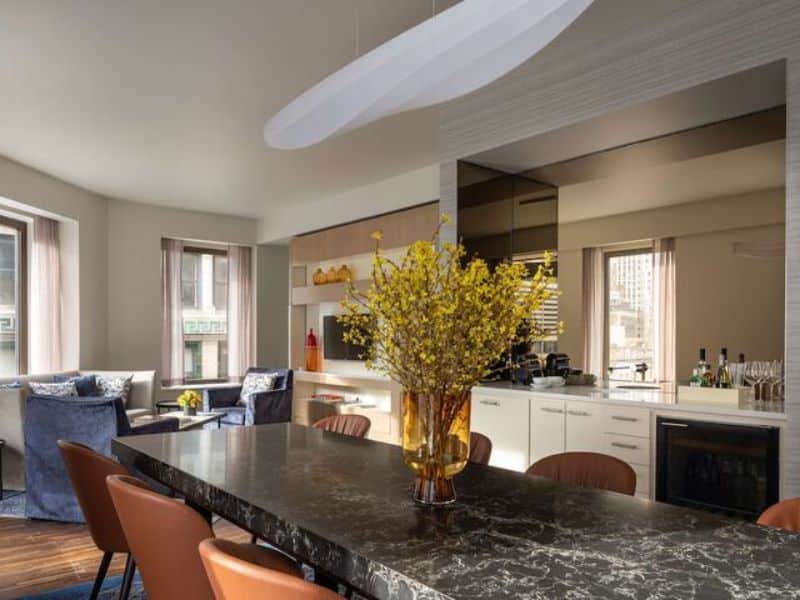 Modern hotel suite interior at Hyatt Centric Wall Street featuring a stylish dining area with a marble table, decorative flower vase, and a well-equipped kitchen area, emphasizing luxury and comfort in New York City's Financial District.