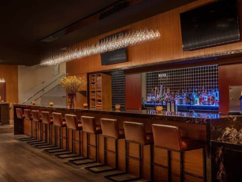 Stylish hotel bar at Hyatt Centric Wall Street featuring a sleek counter, modern seating, and an array of illuminated liquor bottles.