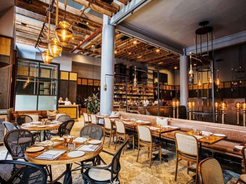 Stylish dining area in Hyatt Union Square New York featuring modern decor, wooden beams, and ambient lighting, showcasing tables set for guests and a bar in the background.