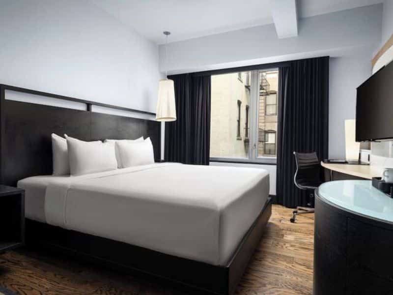 Stylish hotel room at Hyatt Union Square New York featuring a queen bed, modern furnishings, large window with city view, and workspace with desk and chair.
