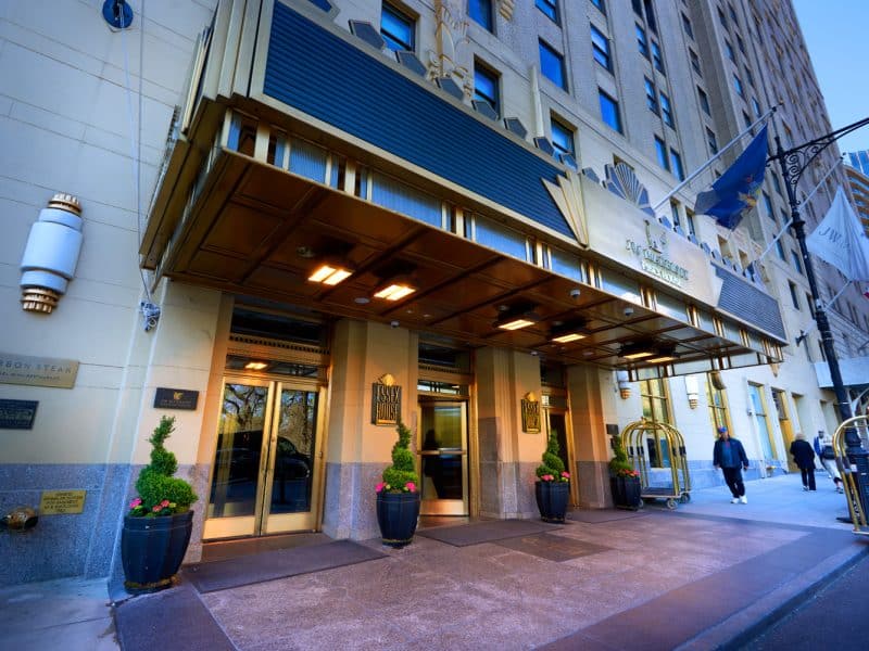 JW Marriott Essex House entrance featuring Art Deco architecture, gold accents, and potted greenery, located near Central Park in New York City.
