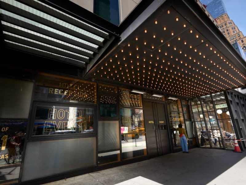Hotel Eventi entrance with illuminated marquee, featuring "Hotel Reception" and "Hotel Event" signage, stylish modern design, and a guest at the door, located in Chelsea, New York City.