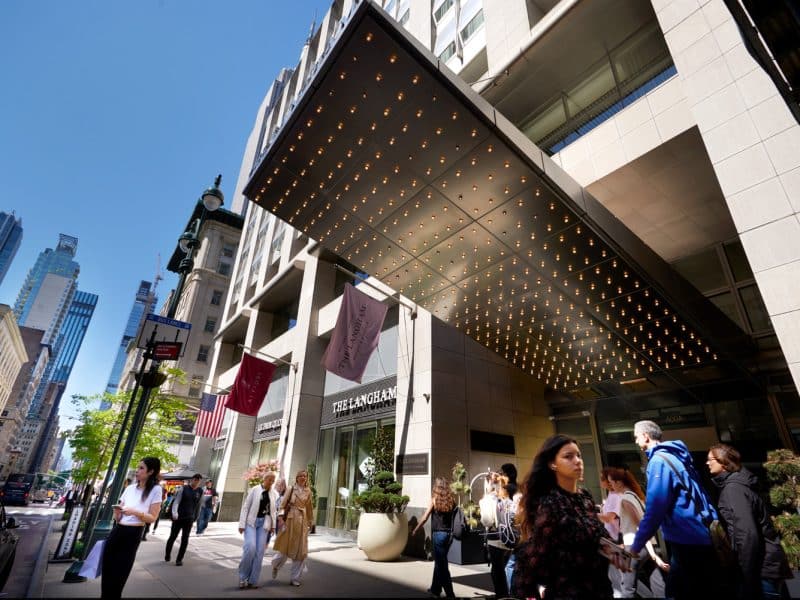 The Langham New York, Fifth Avenue entrance with marquee lights, pedestrians walking, and nearby cityscape.