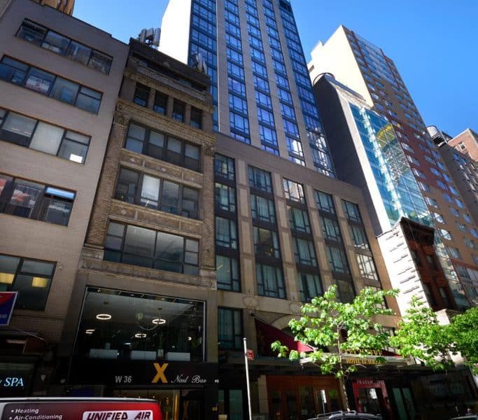 Executive Hotel Le Soleil New York exterior showcasing a blend of historic and modern architecture in Midtown Manhattan, featuring large windows and nearby greenery.