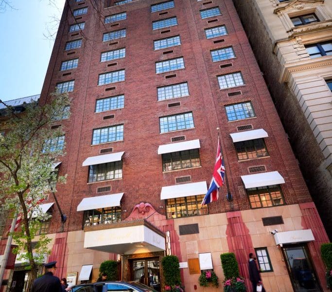 The Lowell boutique hotel exterior, showcasing red brick facade, large windows, and British flag, located on a tree-lined street near Central Park, emphasizing luxury and elegance.