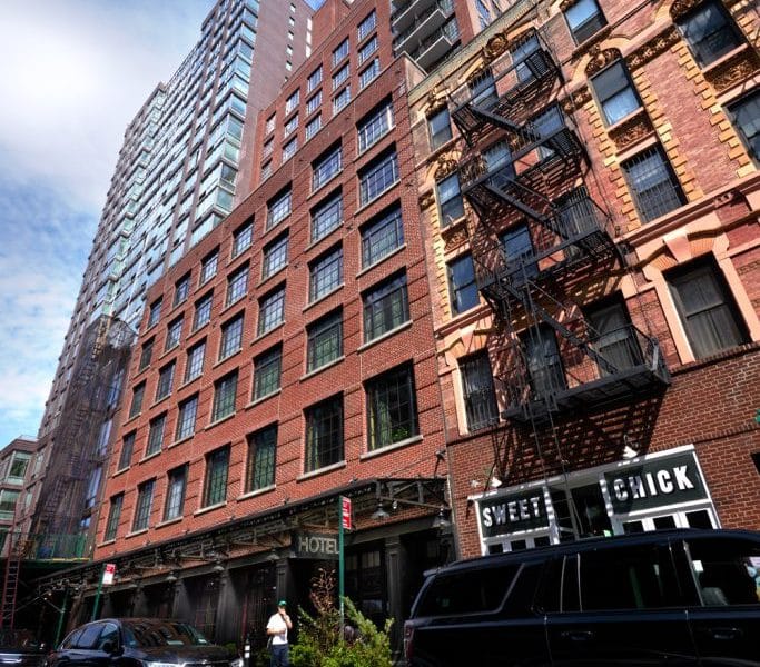 Ludlow Hotel exterior in Manhattan's Lower East Side, showcasing a blend of modern and historic architecture, with nearby restaurant Sweet Chick visible, emphasizing the hotel's trendy location.