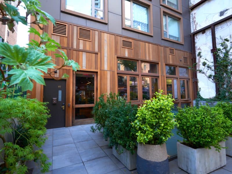 Entrance of Made Hotel featuring modern wooden facade, surrounded by greenery and planters, showcasing the boutique hotel's stylish design in Manhattan's NoMad neighborhood.