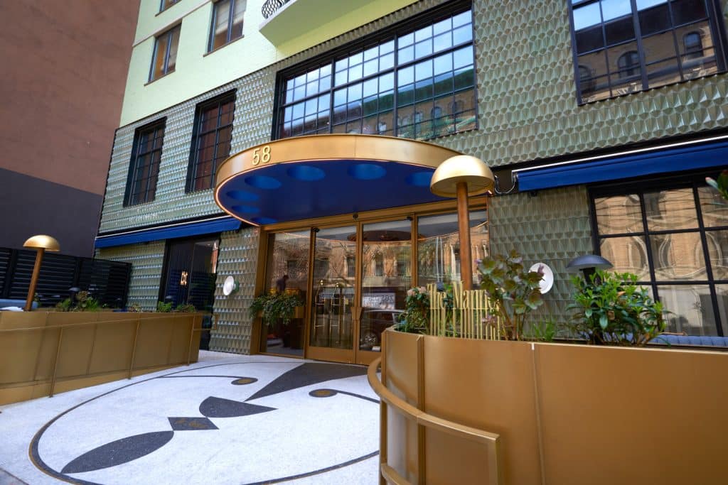 Chic entrance of The Manner Soho boutique hotel featuring modern design, gold accents, and lush greenery, located in Manhattan's SoHo neighborhood.