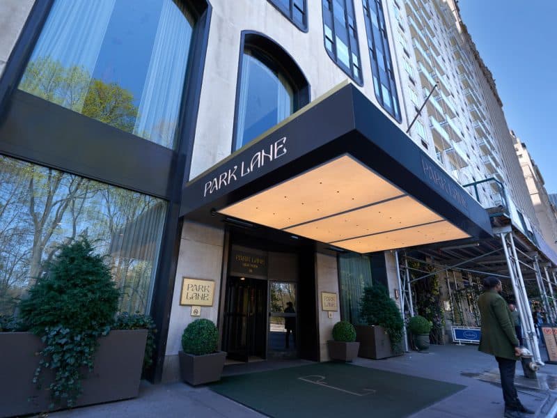 Entrance of Park Lane New York hotel featuring elegant signage, lush greenery, and a welcoming atmosphere, showcasing luxury accommodations near Central Park.