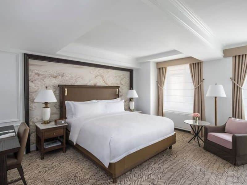 Luxurious hotel room at Ritz-Carlton Central Park featuring a king-size bed, elegant decor, natural light from large windows, and modern furnishings, ideal for travelers seeking sophistication and comfort in New York City.