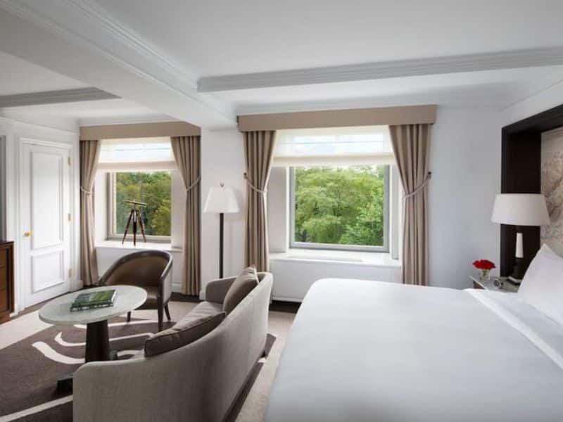 Luxury hotel room at Ritz-Carlton Central Park featuring elegant decor, large windows with park views, a comfortable seating area, and modern furnishings.