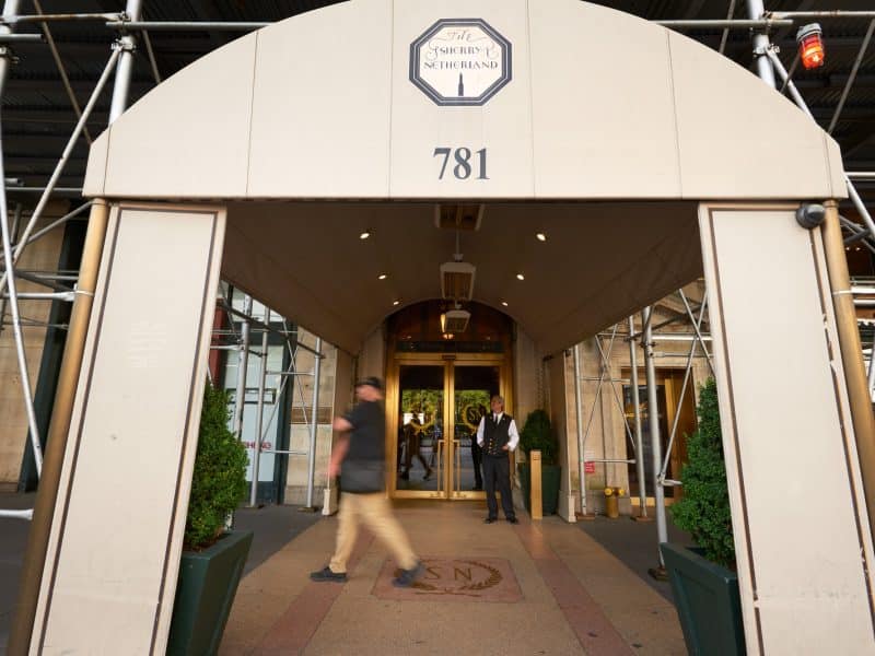 Entrance of The Sherry-Netherland hotel on Fifth Avenue, featuring a canopy, the hotel name and address, and a doorman welcoming guests.