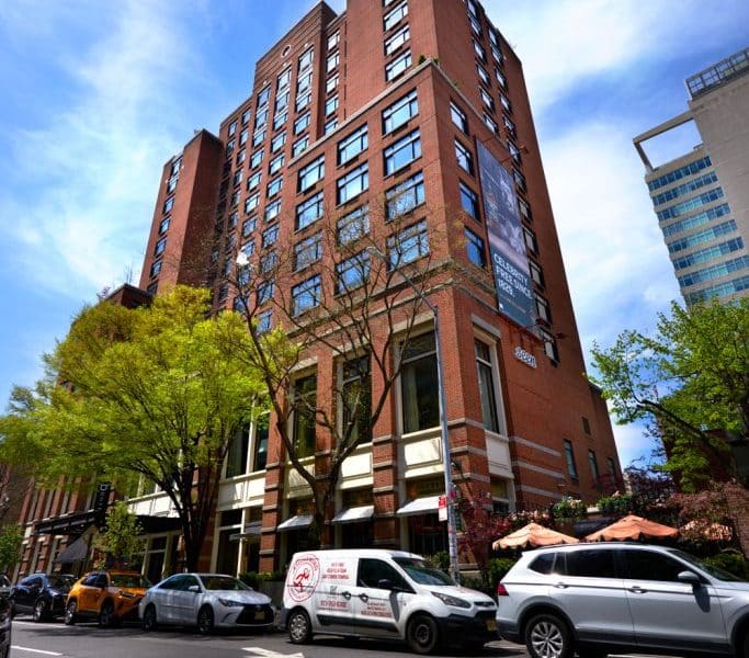 Soho Grand Hotel exterior view, showcasing its industrial-chic design, surrounded by greenery and parked vehicles, located in Manhattan's SoHo neighborhood.