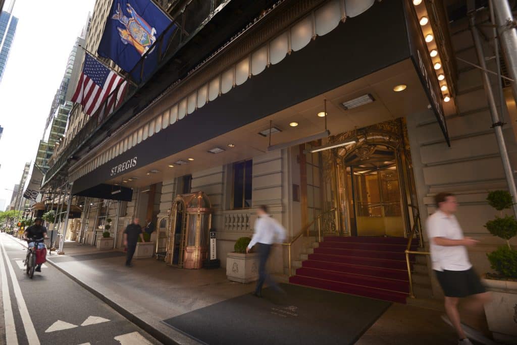 St. Regis New York entrance with luxury decor, American flag, and guests arriving, showcasing the hotel's elegance and prime Midtown Manhattan location.