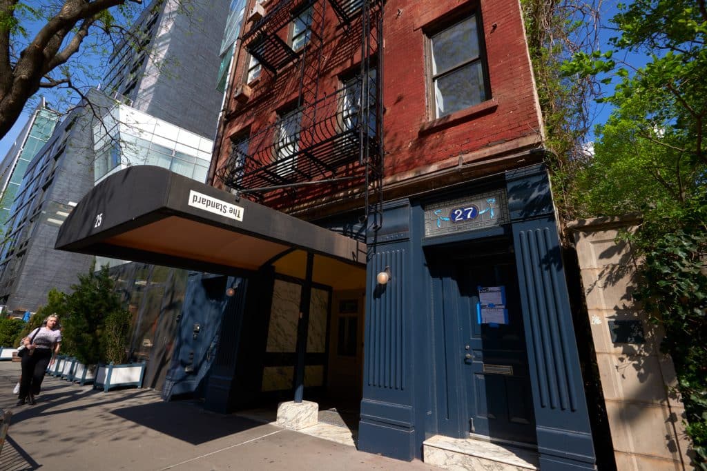 The Standard, East Village hotel entrance featuring modern design, with a visible sign, adjacent buildings, and greenery, located in Manhattan's vibrant East Village.