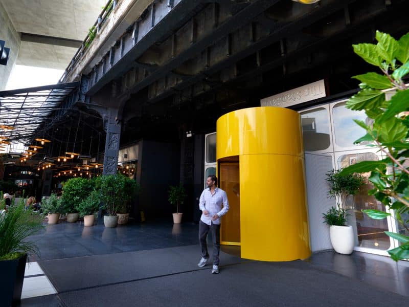 Man exiting the vibrant yellow entrance of The Standard, High Line hotel, showcasing modern architecture and lush greenery in Manhattan's Meatpacking District.