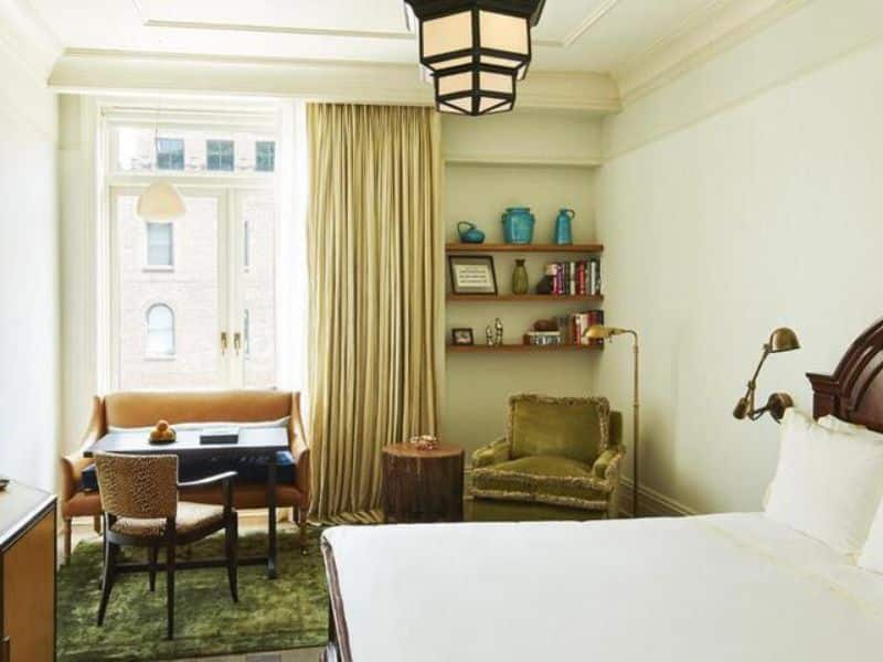 Stylish hotel room at The Greenwich Hotel featuring a cozy seating area, wooden furniture, and natural light from large windows, emphasizing luxury and comfort in Tribeca.