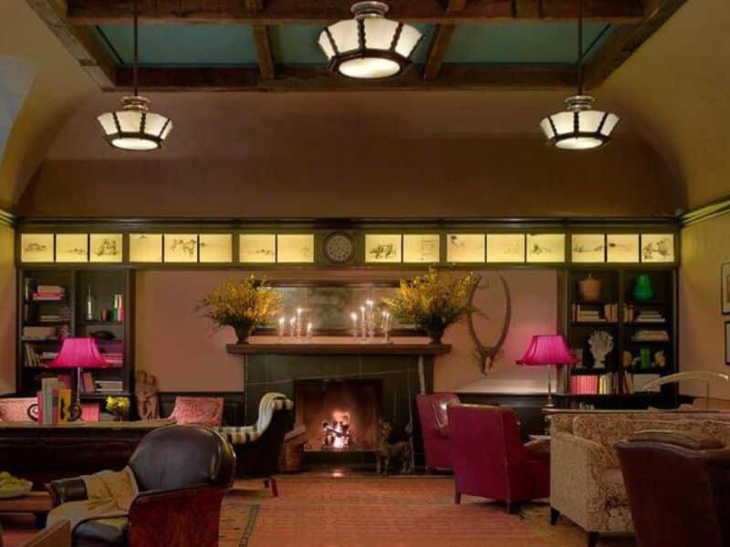 Cozy lounge area in The Greenwich Hotel featuring a fireplace, elegant furnishings, warm lighting, and decorative floral arrangements.