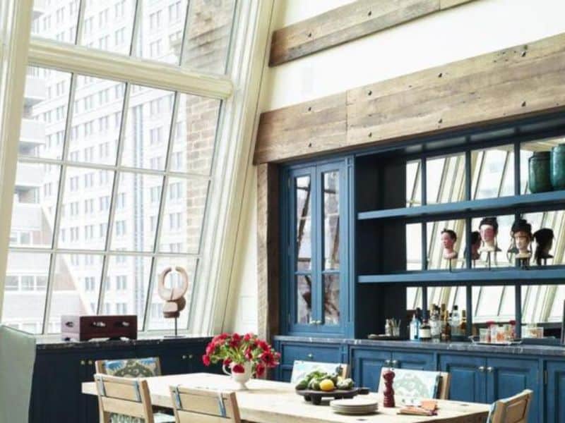 Stylish dining area in The Greenwich Hotel featuring large windows, blue cabinetry, and a wooden table adorned with flowers and fruit, highlighting the boutique hotel's sophisticated and intimate ambiance.