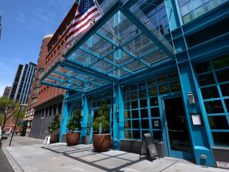 Warren Street Hotel entrance featuring modern glass architecture, American flag, and decorative planters in Tribeca, showcasing the hotel's chic and vibrant atmosphere.