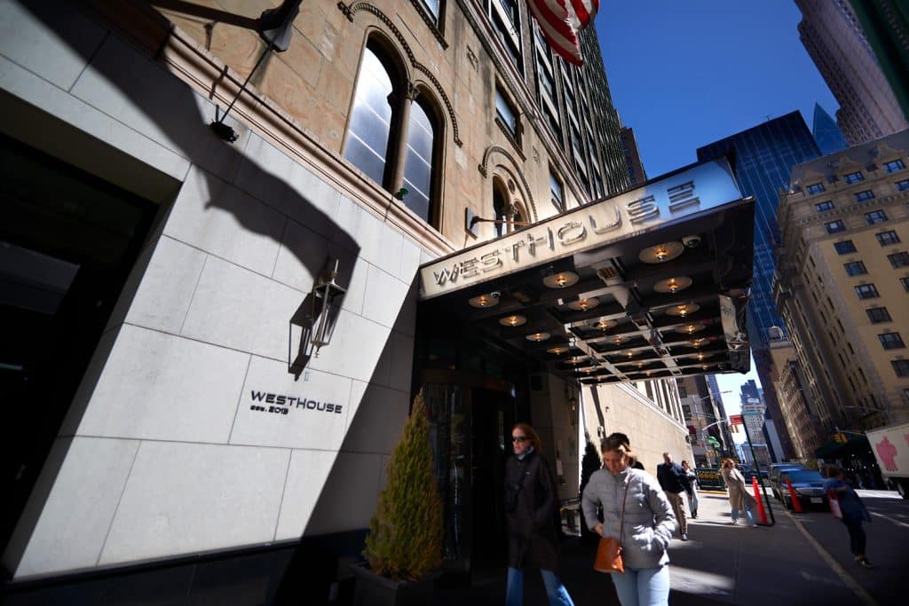 WestHouse New York hotel entrance with elegant signage, guests walking outside, and Midtown Manhattan skyline in the background.
