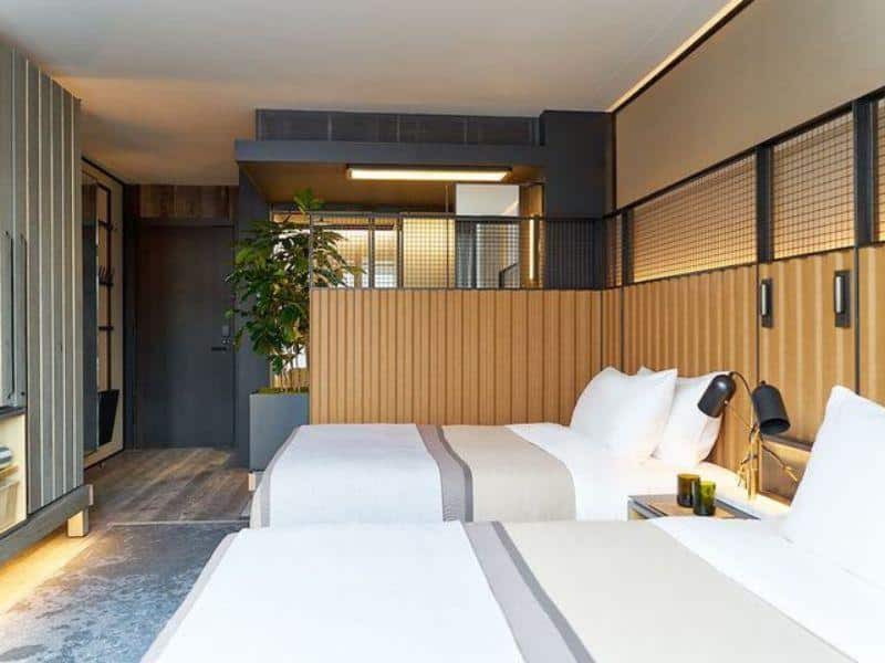 Modern hotel room at 1 Hotel Brooklyn Bridge featuring two beds, eco-friendly design elements, wooden accents, and greenery, illustrating luxury and sustainability.