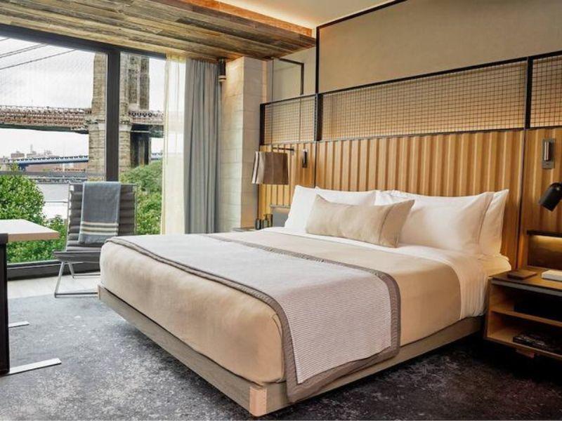 Luxurious hotel room at 1 Hotel Brooklyn Bridge with eco-conscious design, featuring a king-sized bed, modern decor, and views of the Brooklyn waterfront and bridge.