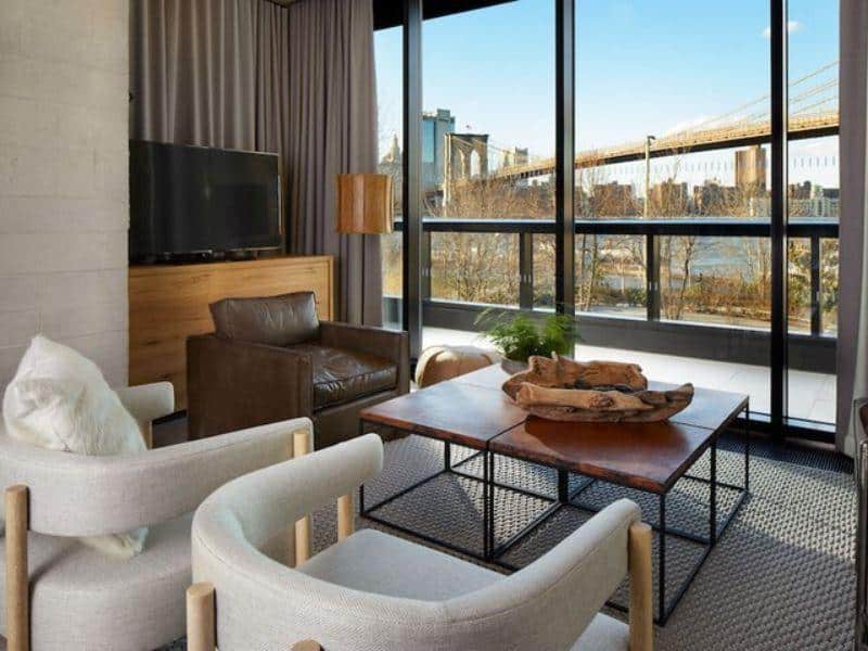 Stylish hotel room at 1 Hotel Brooklyn Bridge featuring modern furnishings, large windows with views of the Brooklyn Bridge and waterfront, and a cozy atmosphere.