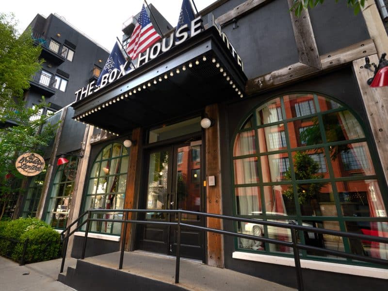 The Box House Hotel entrance featuring large arched windows, wooden accents, and American flags, located in Greenpoint, Brooklyn, showcasing the hotel's unique boutique style.