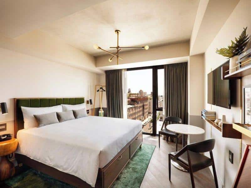 Stylish hotel room at The Hoxton, Williamsburg featuring a queen bed, modern decor, large windows with city views, and a cozy seating area.