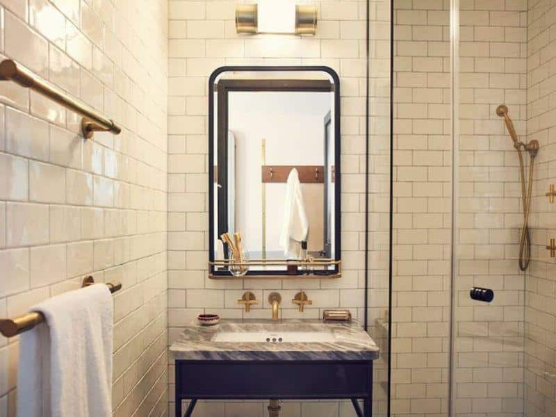 Modern bathroom with marble sink, gold fixtures, large mirror, and glass shower, showcasing The Hoxton, Williamsburg's stylish design and amenities.