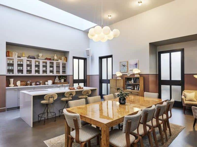 Stylish dining area with a large wooden table, modern pendant lighting, and a kitchen space featuring open shelves, located in The Hoxton, Williamsburg boutique hotel.