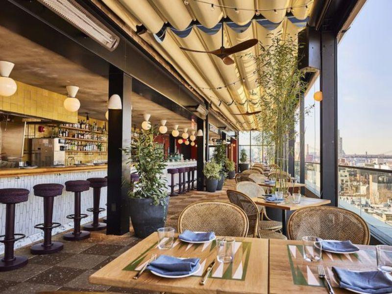 Rooftop bar and restaurant interior at The Hoxton, Williamsburg, featuring modern design, greenery, and views of the Manhattan skyline.