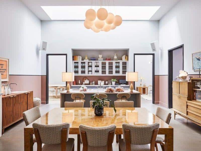 Stylish dining area in The Hoxton, Williamsburg featuring a wooden table, modern lighting, and an open kitchen with pastries and coffee service, reflecting the hotel's trendy and inviting atmosphere.
