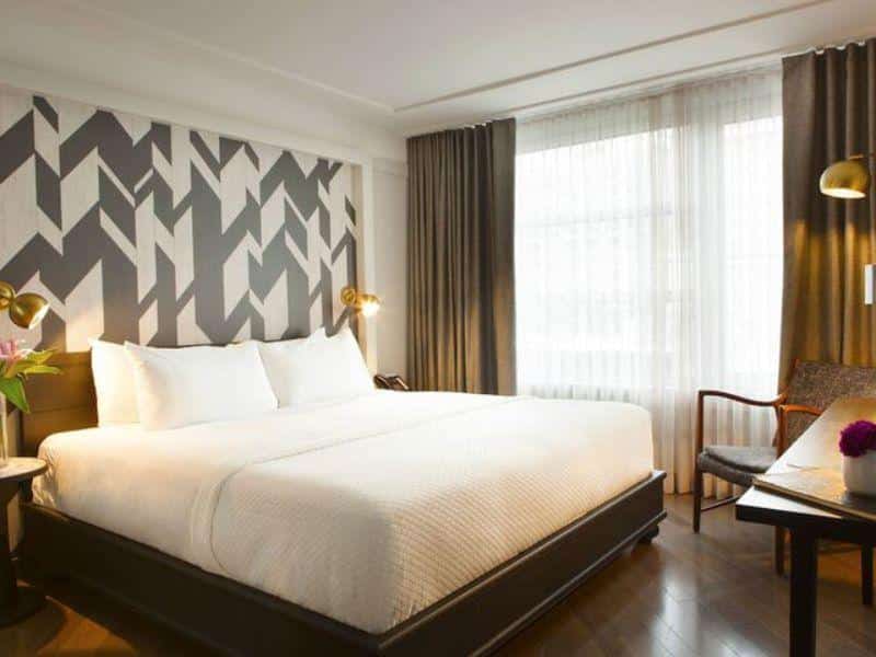 Stylish hotel room at The Tillary Hotel Brooklyn featuring a king-size bed, geometric accent wall, modern furnishings, and ample natural light.
