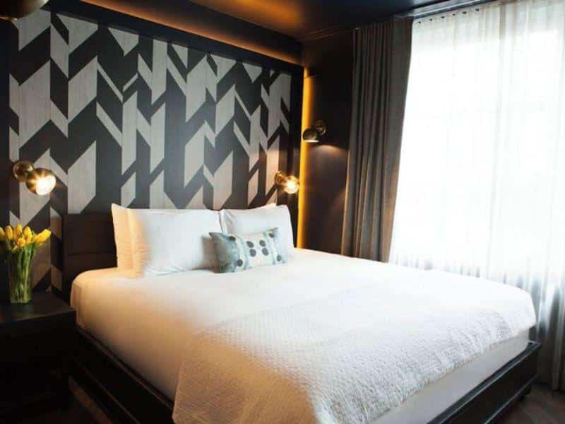 Stylish hotel room at The Tillary Hotel Brooklyn featuring a modern design, a large bed with decorative pillows, and a patterned accent wall, ideal for leisure and business travelers.