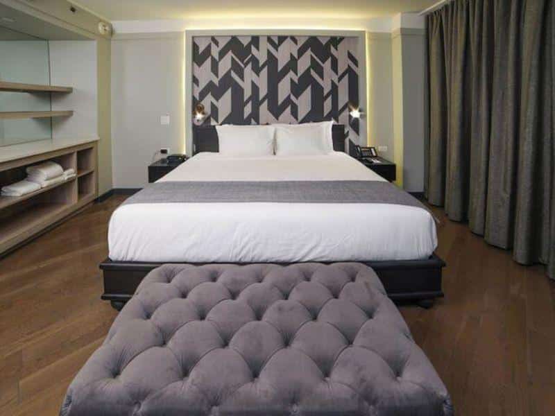 Stylish hotel room at The Tillary Hotel Brooklyn featuring a king-size bed, modern decor, and plush ottoman, showcasing amenities for business and leisure travelers.