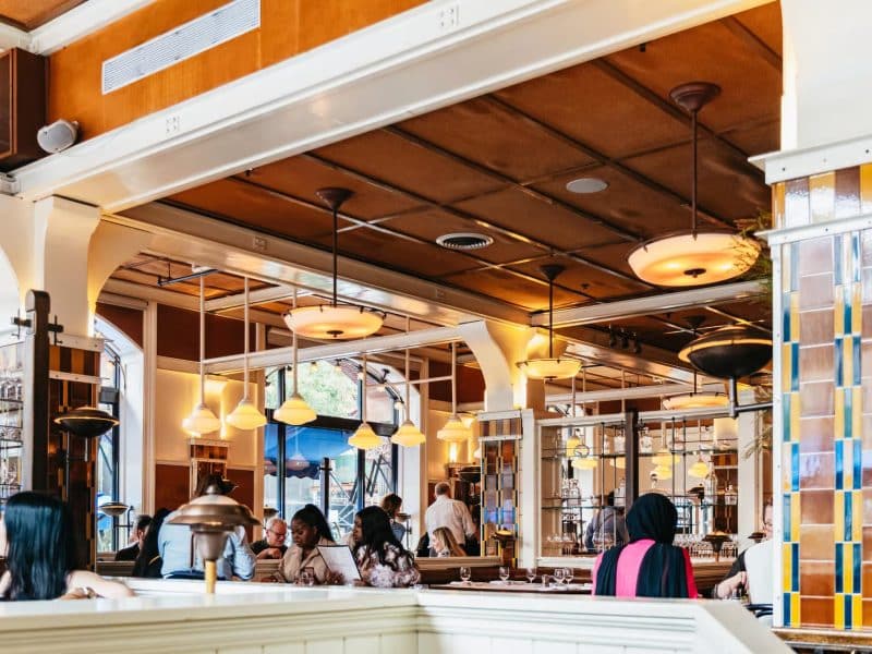 Charming interior of Lafayette Grand Caf&eacute; & Bakery, featuring diners enjoying meals in a cozy atmosphere, showcasing elegant lighting and decor, relevant to Taylor Swift's NYC hotspots tour.